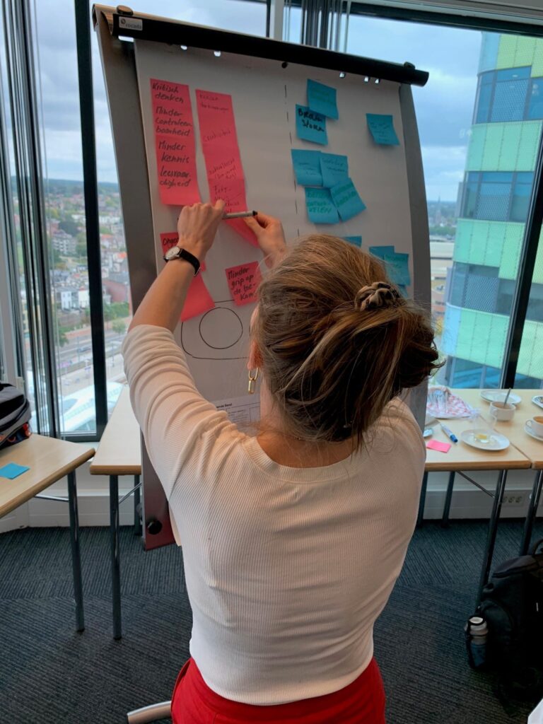 Docent plakt post-its op een flipover tijdens de lopende band opdracht in Arnhem