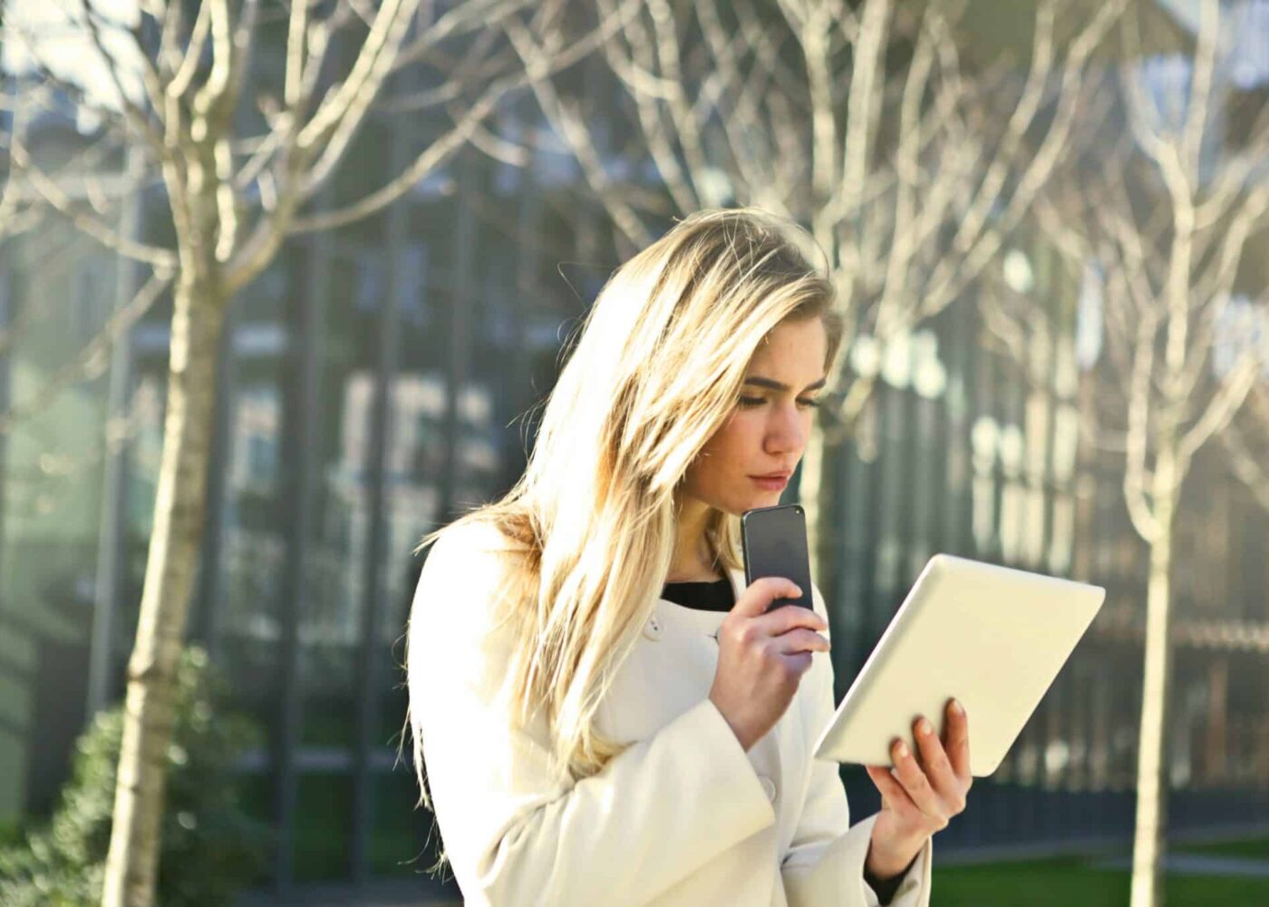 Studente voor school met mobiel in de hand en kijkend op haar iPad