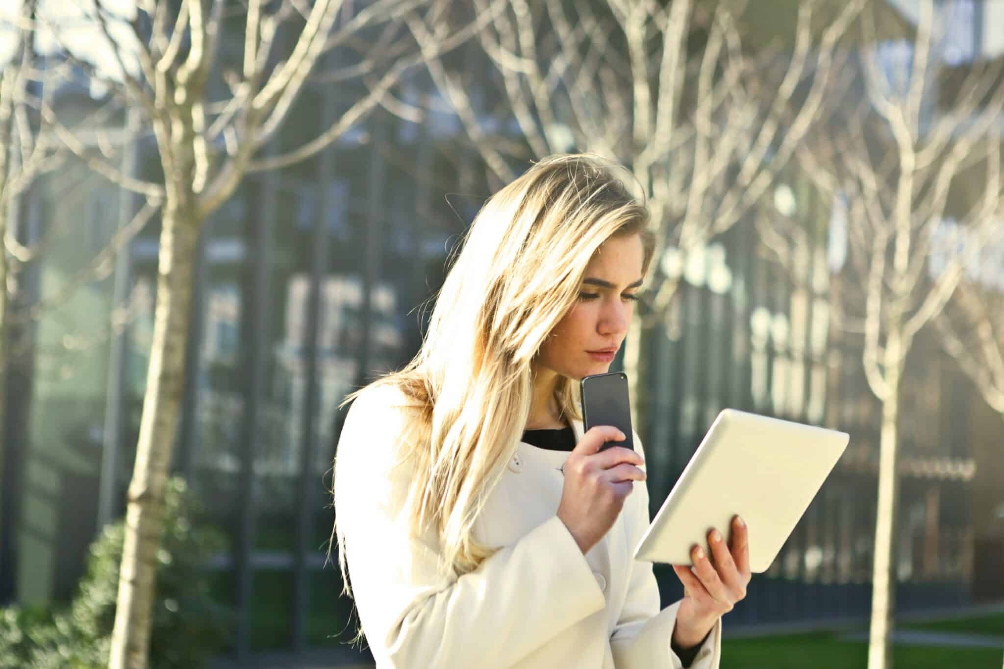 Studente voor school met mobiel in de hand en kijkend op haar iPad