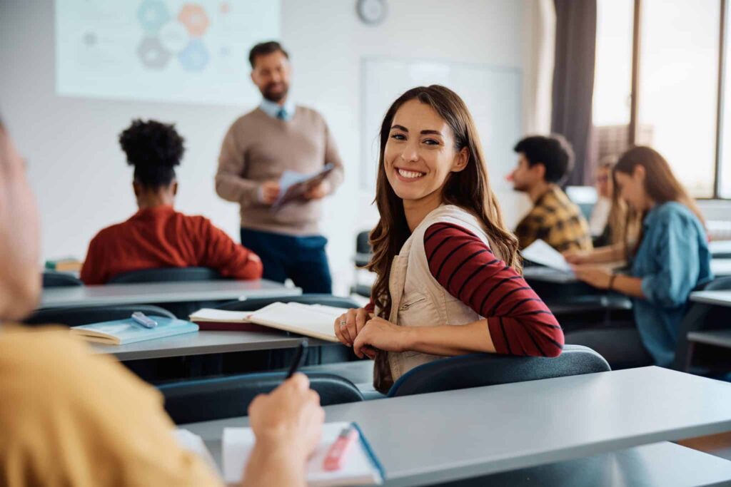 Blije student die lacht in de camera en zit in de klas. Leraar staat voor de klas